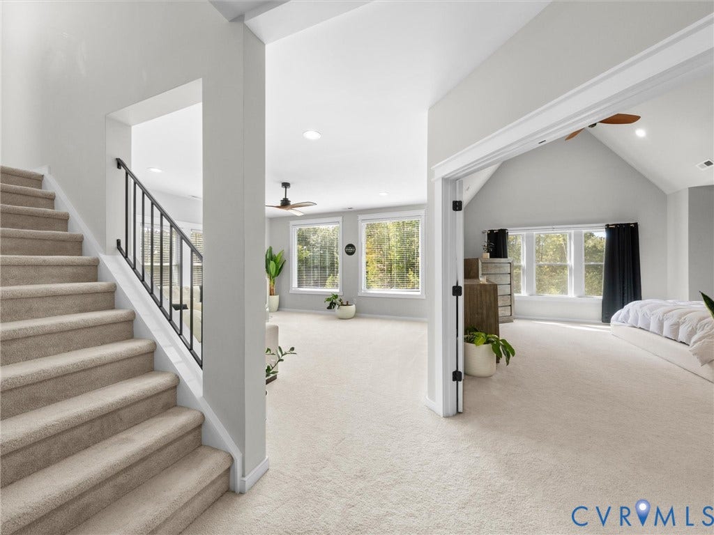 Carpeted staircase with black metal railing, vaulted ceilings, and multiple large windows
