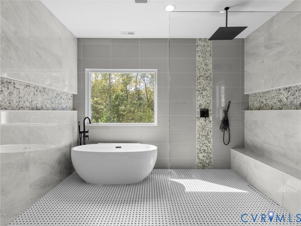 Freestanding soaking tub with floor-mounted faucet, walk-in shower with rain head and handheld fixtures, built-in shower bench, and pebble tile accents