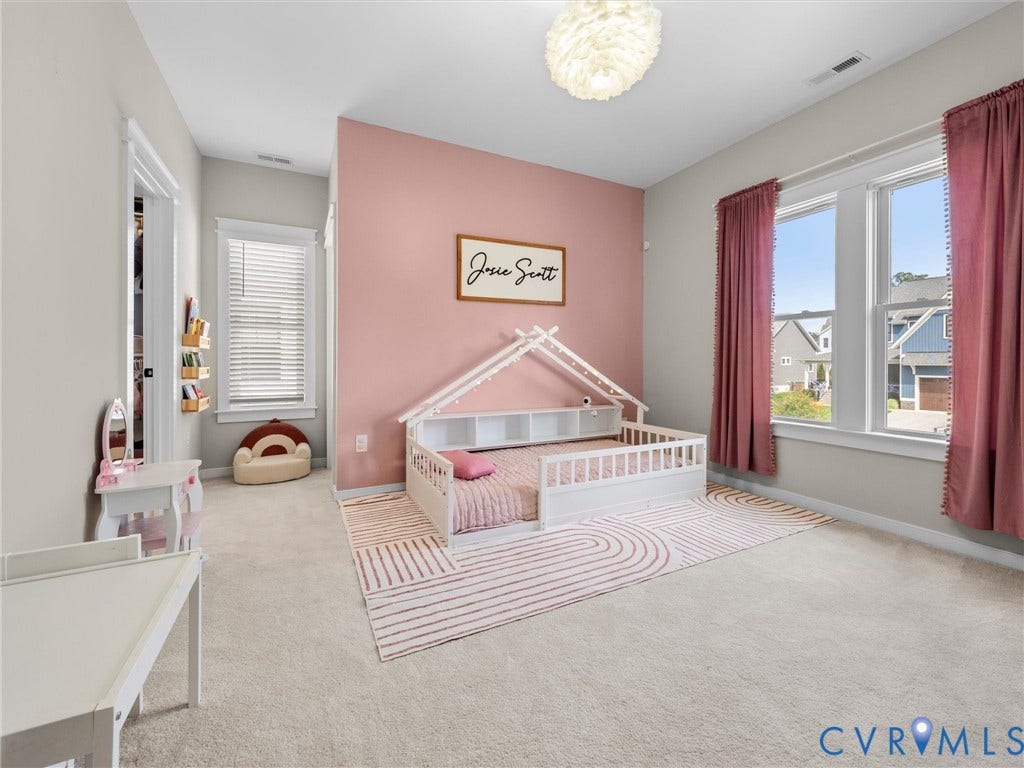 Carpeted flooring throughout, with a single window featuring blinds and a second double window with curtains