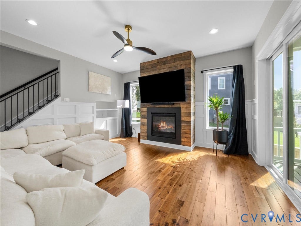 Hardwood flooring throughout, a gas fireplace with a wood-finish surround, and a ceiling fan with integrated lighting