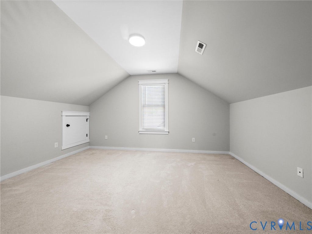 Sloped ceiling with recessed lighting, light-toned carpet flooring, window with blinds, and white trim details