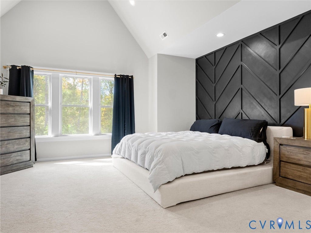 Vaulted ceiling, recessed lighting, accent wall with geometric paneling, triple window, and light-colored carpeting