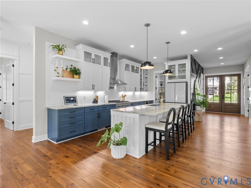 Expansive kitchen featuring wood-finish flooring, a large island with seating, pendant lighting, two-tone cabinetry, and double glass-paneled entry doors