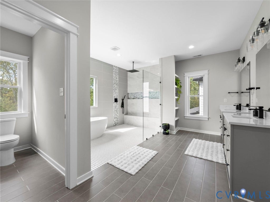 Expansive bathroom featuring dual vanities with white countertops, a freestanding tub, and a glass-enclosed shower with a rainfall showerhead