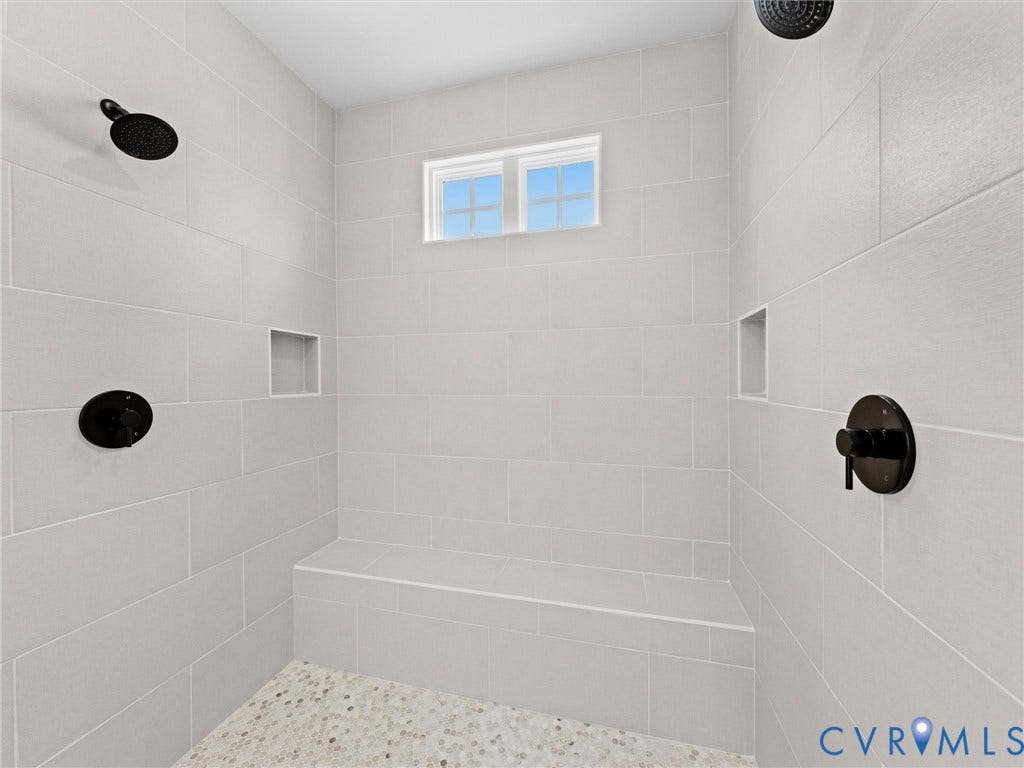3719 Bellstone Drive, Midlothian, VA 23112 Spacious shower with light-toned tiled walls, dual matte black shower heads, integrated shower bench, two recessed storage niches, and a high-set window