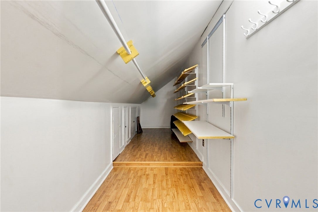 9015 Wood Sorrel Drive, Henrico, VA 23229 Sloped ceiling storage space featuring wood-finish flooring, adjustable wall-mounted shelving units, a fixed garment rod, and built-in wall access panels