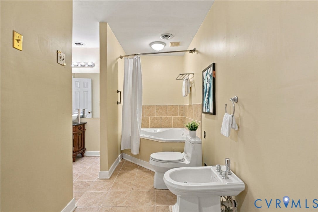 9015 Wood Sorrel Drive, Henrico, VA 23229 Corner soaking tub with tile surround, white pedestal bidet, ceramic tile flooring, and wall-mounted metal towel rack