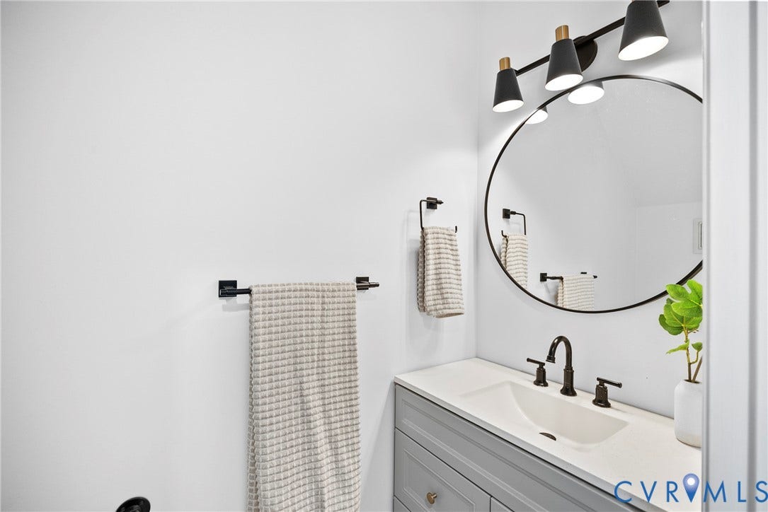 8406 Chandon Court, Chesterfield, VA 23838 Gray vanity with shaker-style door fronts, integrated sink, bronze-finish faucet, and circular mirror