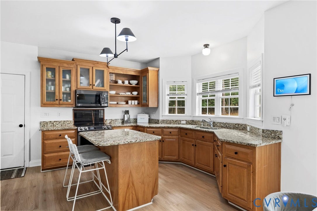 8406 Chandon Court, Chesterfield, VA 23838 Chef's kitchen featuring warm wood cabinetry with glass-front upper cabinets, granite countertops, a spacious island with seating, stainless steel appliances, and abundant natural light from multiple windows with plantation shutters