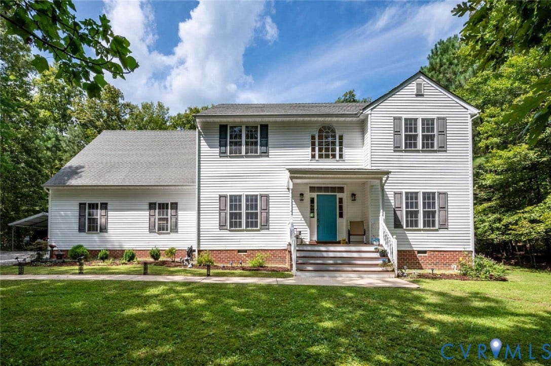 White siding exterior with a front porch, bright teal entry door, gray shutters, and established landscaping