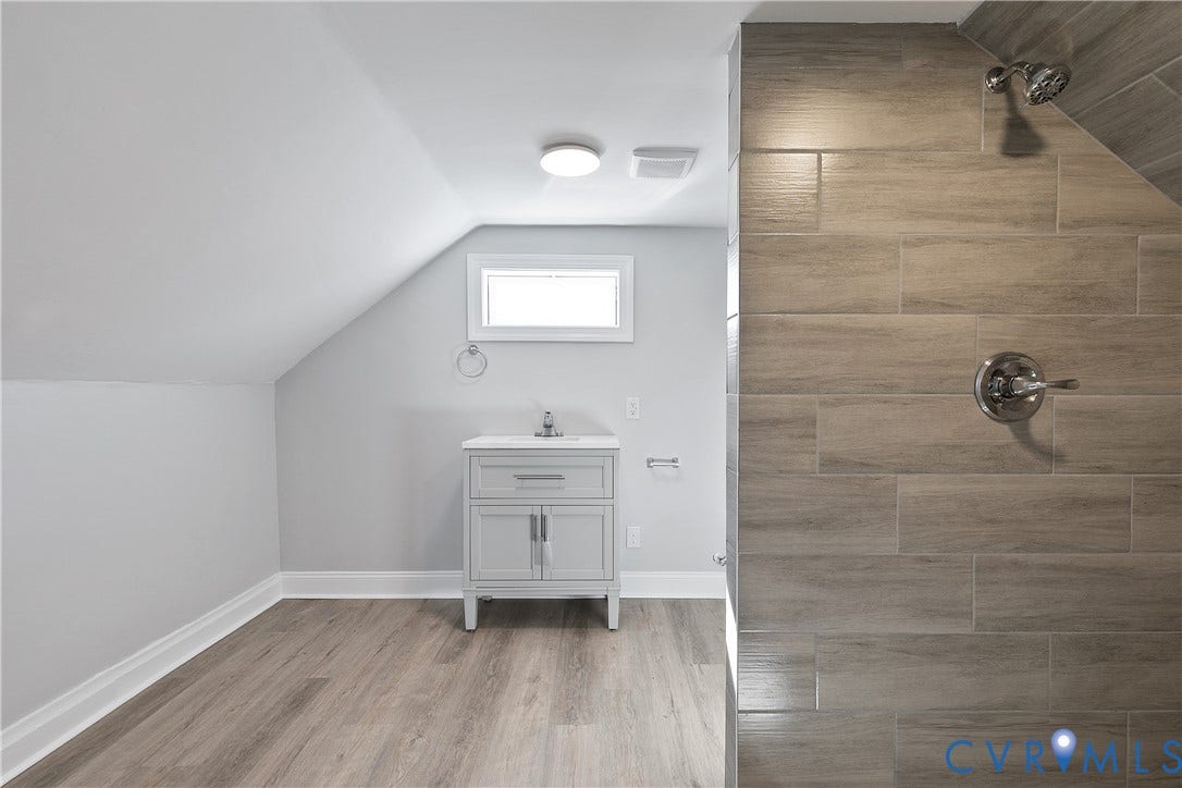 1305 Overlook Street, Richmond, VA 23224 Sloped ceiling, wood-finish flooring, white vanity with integrated sink, rectangular window, and fully tiled shower with chrome fixtures