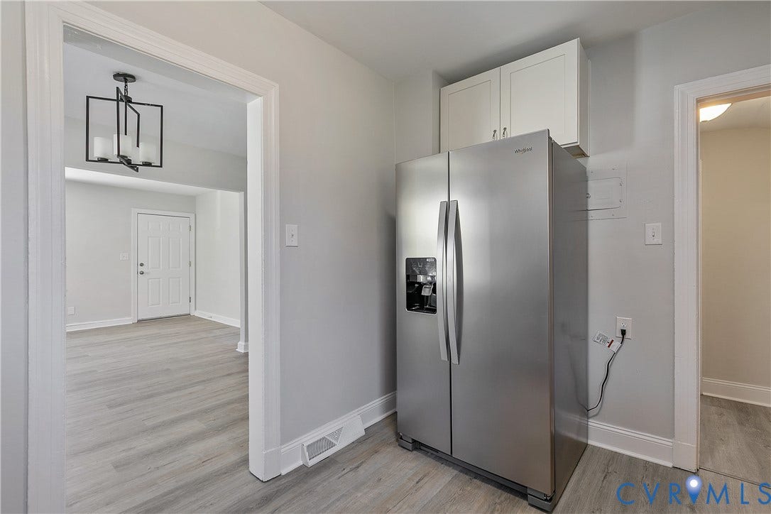 1305 Overlook Street, Richmond, VA 23224 Stainless steel side-by-side refrigerator, white upper cabinetry, light wood-finish flooring, white door and trim, and a contemporary black chandelier