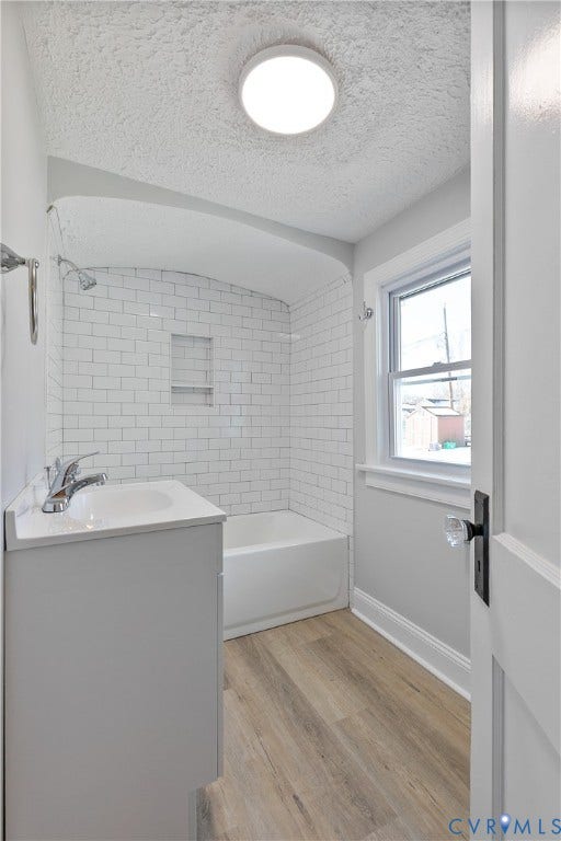 1305 Overlook Street, Richmond, VA 23224 Bathroom featuring a white subway tile shower, built-in shower niche, white soaking tub, wood-finish flooring, and a single-pane window