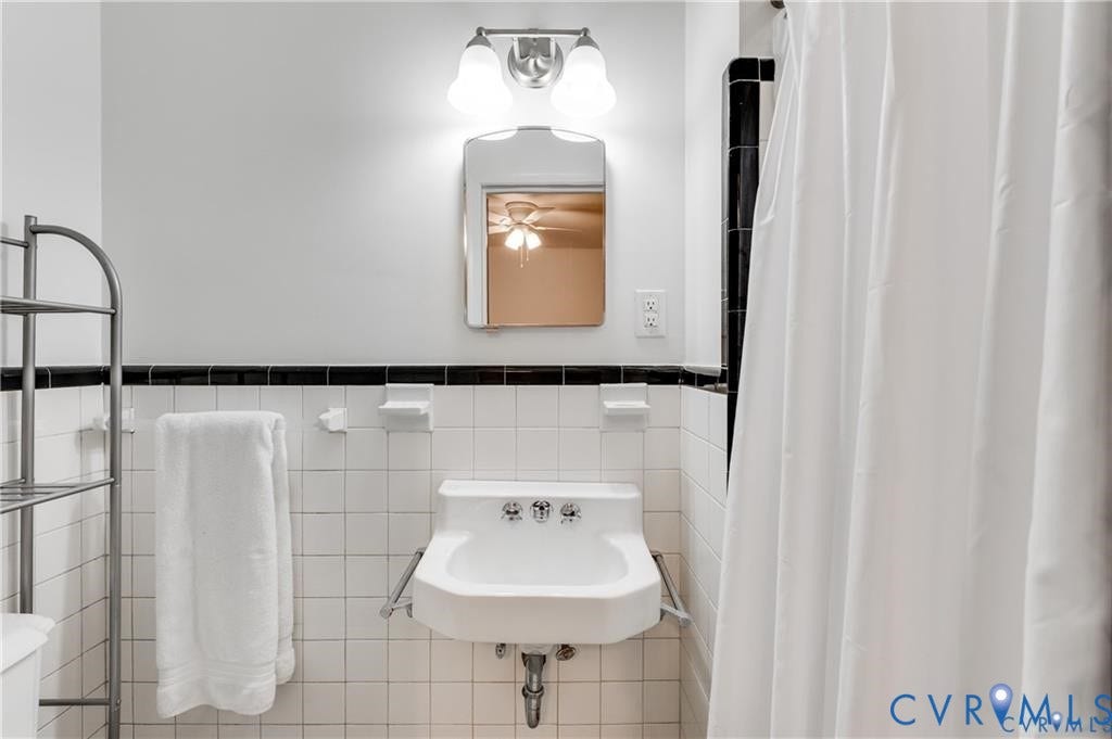2304 Buckingham Avenue, Henrico, VA 23228 Pedestal sink with chrome fixtures, wall-mounted mirror, and white tiled walls with a black accent border