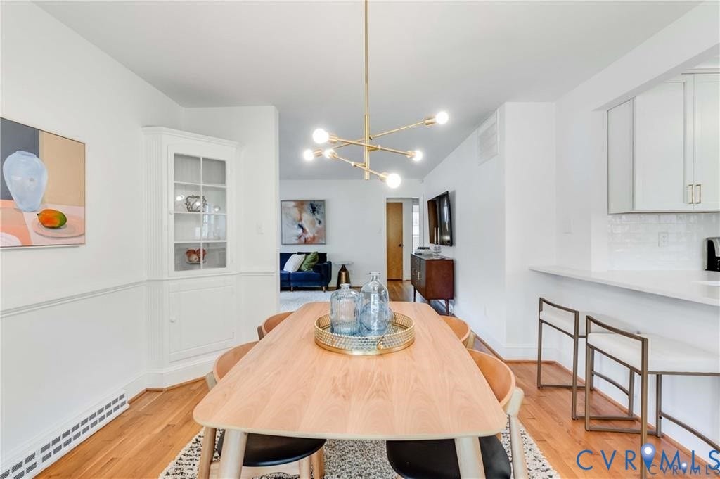 2304 Buckingham Avenue, Henrico, VA 23228 Hardwood flooring, a built-in corner cabinet with glass-front doors, a modern linear light fixture, and a kitchen pass-through with a breakfast bar