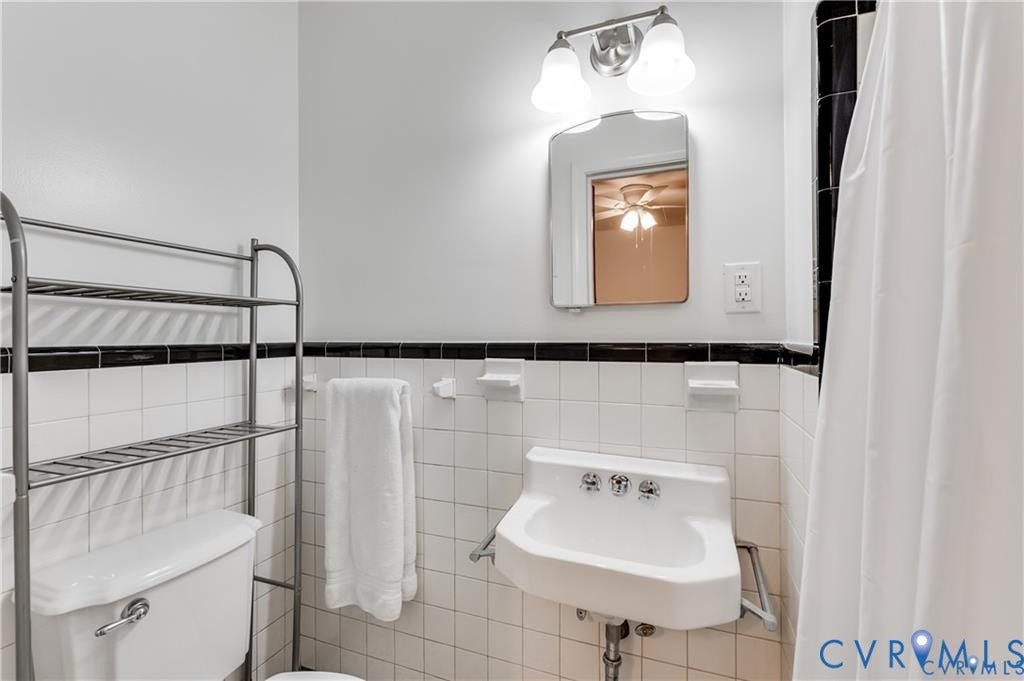2304 Buckingham Avenue, Henrico, VA 23228 White tile walls with black trim, wall-mounted sink, wall-mounted mirror, and vanity light fixture