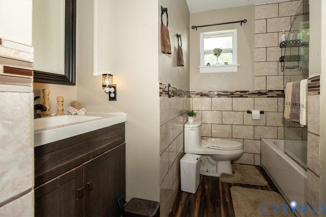 5510 Alberta Road, Stanwick, Midlothian, VA 23832 Vanity with integrated sink, wood-finish flooring, tiled shower/tub combination, tiled walls with decorative mosaic accents, and a window for natural light