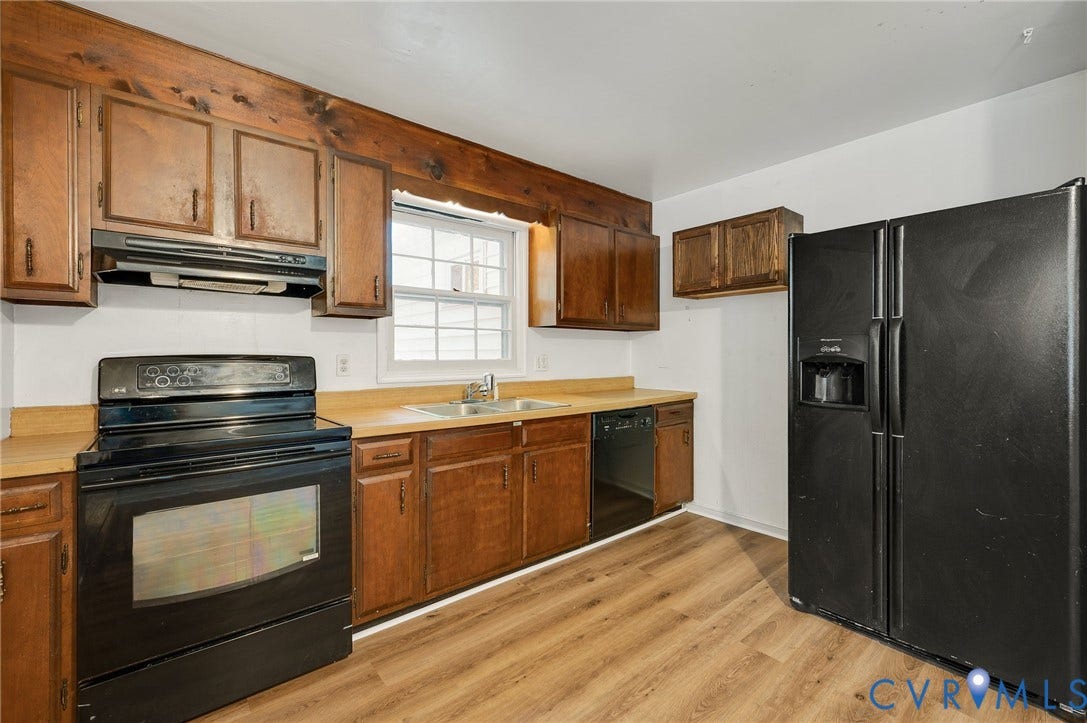 Black appliance suite, wood-finish flooring, wood cabinetry, and a double basin sink with window