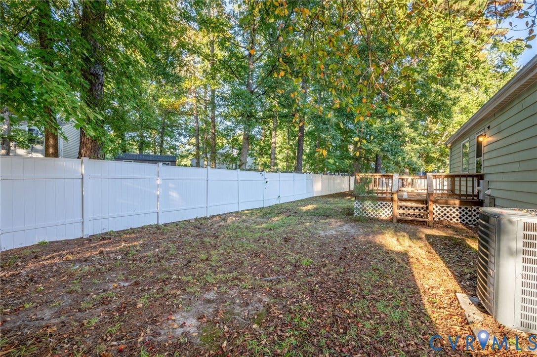 Expansive backyard featuring a white privacy fence, multi-level wood deck, and mature trees