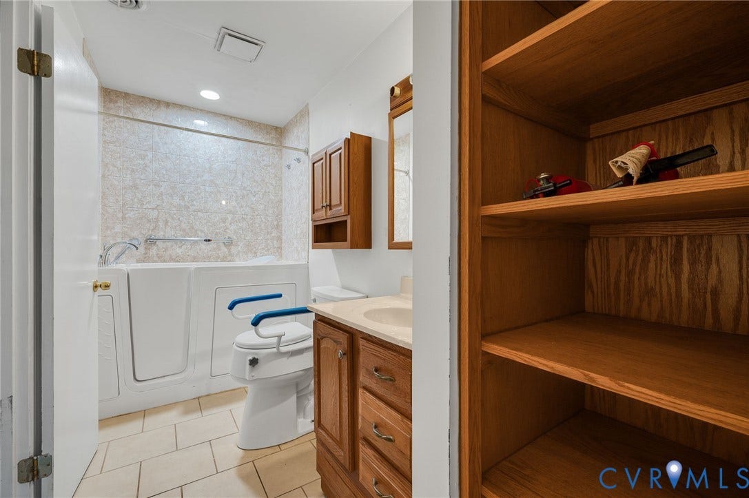 Tile flooring, a walk-in tub with a tiled surround, a vanity with a light-colored countertop, and wood-finish cabinetry