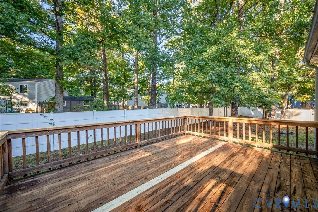 Expansive wood deck with wood railings, overlooking a fenced yard and mature trees