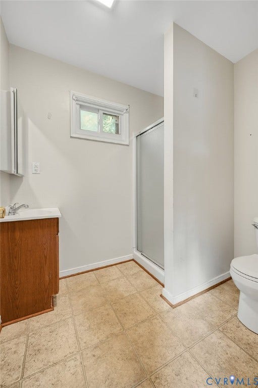 White walls with white trim, a wood-finish vanity with a white countertop, and an enclosed shower with a sliding glass door