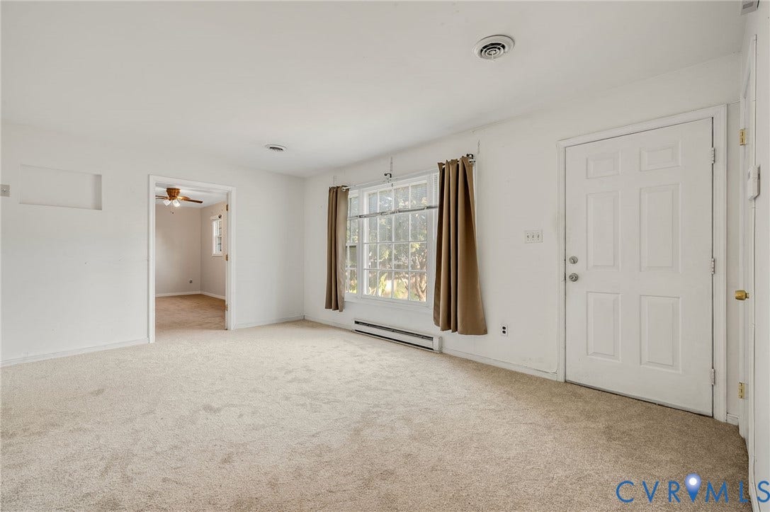 Light-toned carpet flooring, white painted walls, and a multi-pane window with window treatments