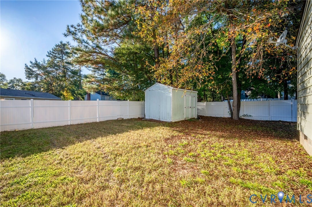 Spacious backyard featuring a storage shed, white privacy fencing, and mature trees