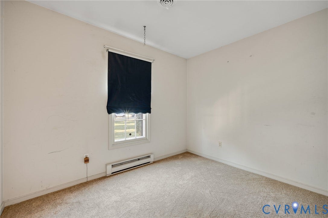 Carpeted flooring, white walls, and a single window with a dark roller shade