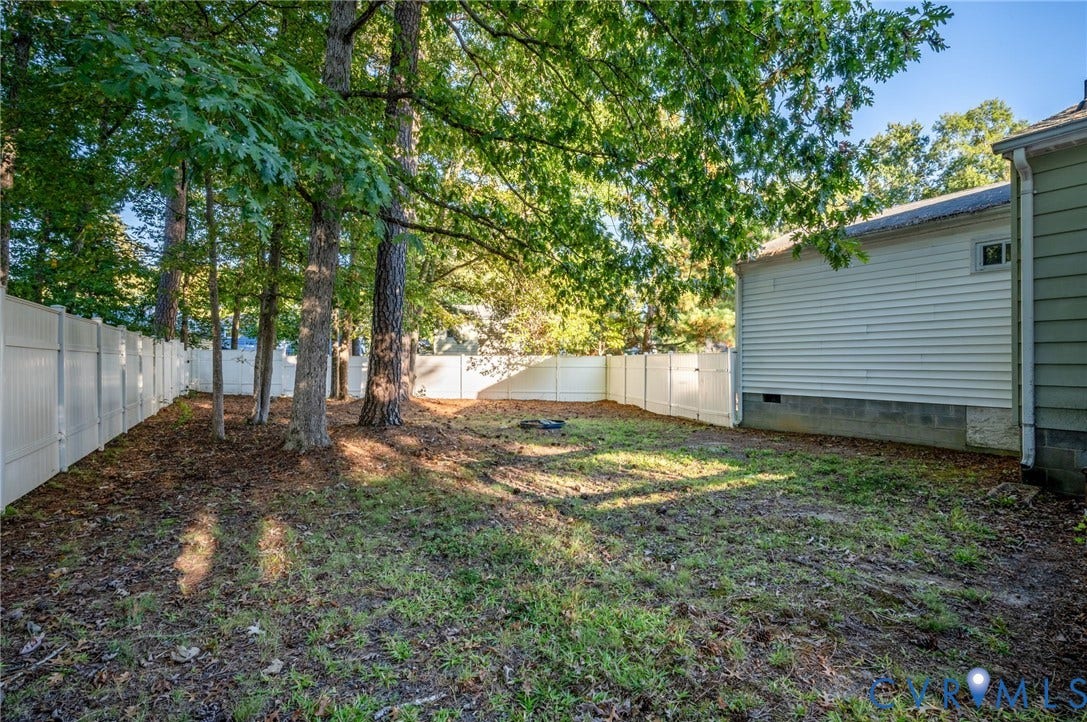 Expansive backyard featuring a privacy fence, mature trees, and a grassy area