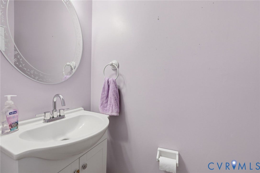 Vanity with integrated sink, chrome faucet, and an oval wall mirror with etched detailing