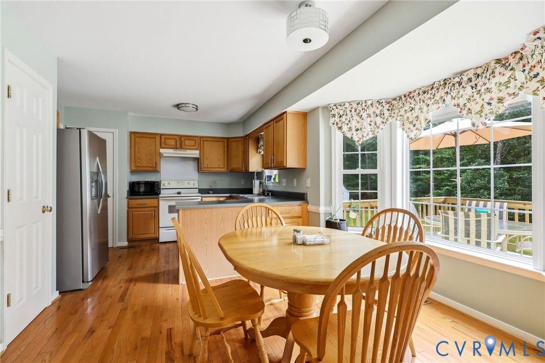 Hardwood flooring, wood cabinetry, stainless steel refrigerator, and a bay window
