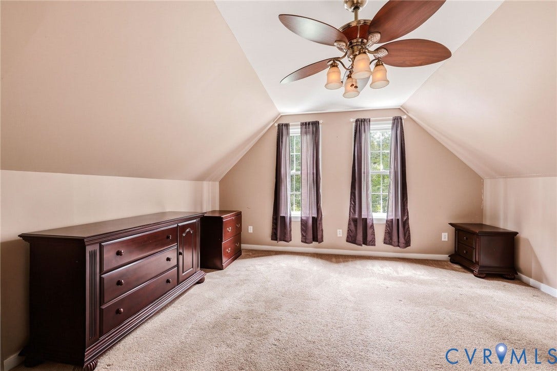 Vaulted ceiling with a multi-blade ceiling fan, two windows, and light-colored carpeting