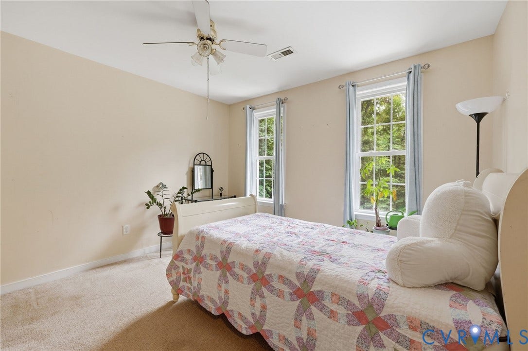 Carpeted flooring, two double-hung windows, ceiling-mounted fan with integrated lighting, and neutral wall tones