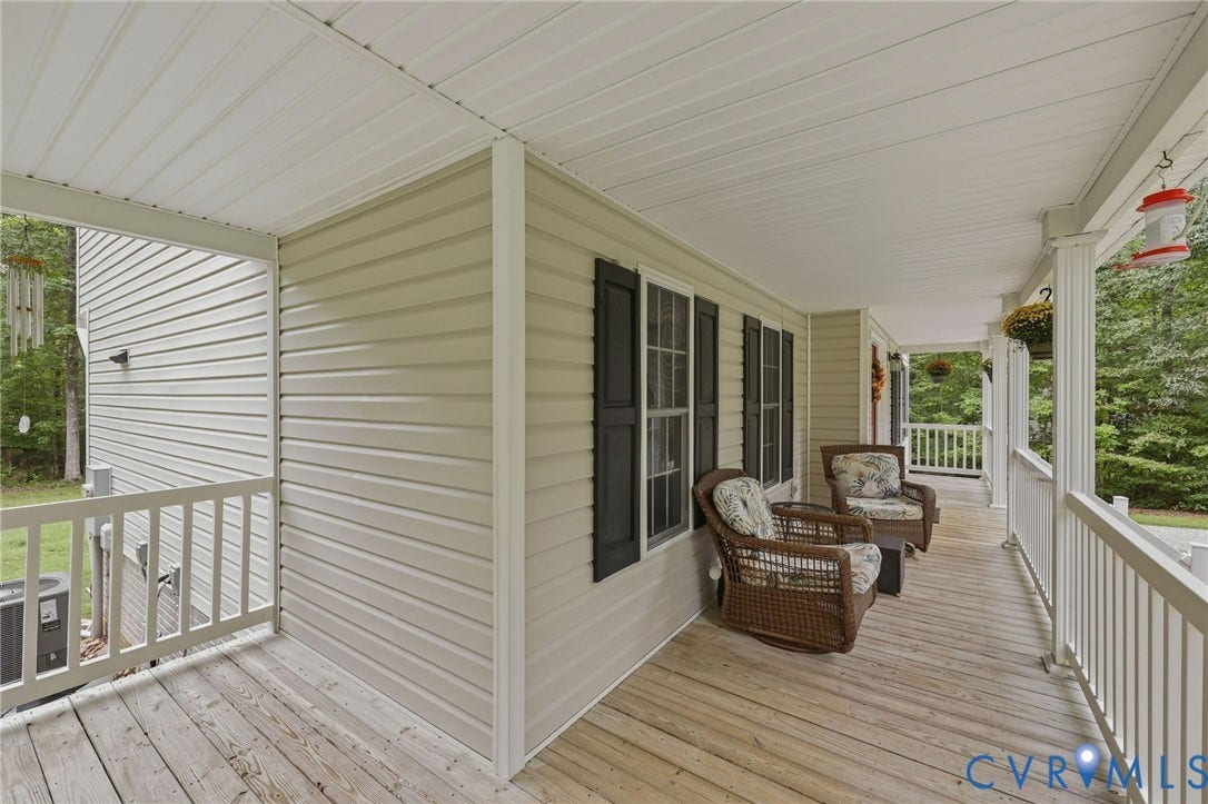 Expansive covered front porch with wood flooring, white railings, and white siding