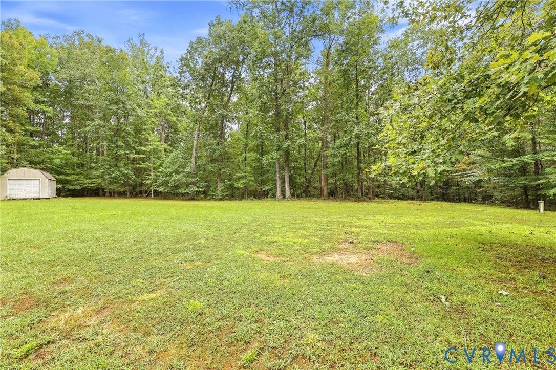 Expansive lawn area bordered by mature trees and a metal storage shed