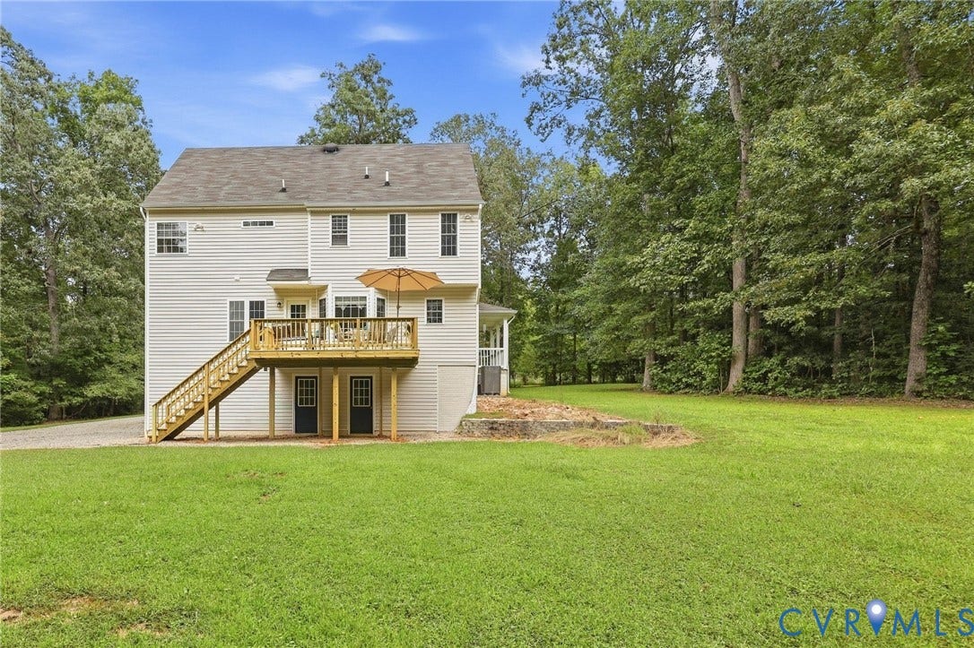 Two-story exterior with vinyl siding, wood-plank deck, and expansive grass lawn