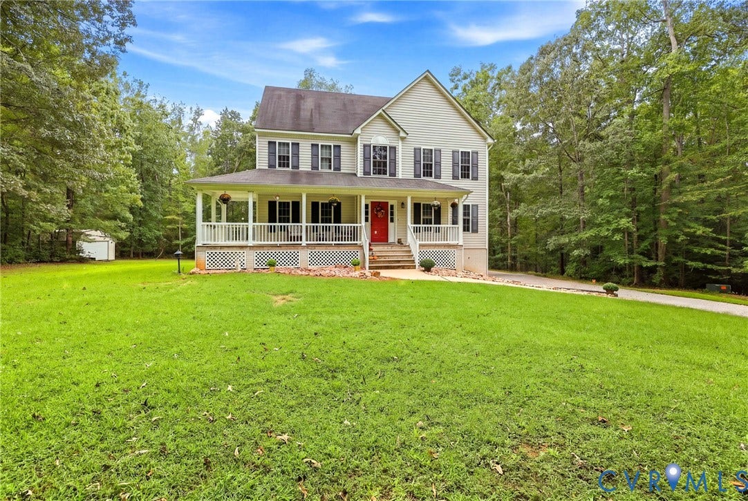 Two-story residential structure with a covered front porch, white railings, and a red entry door