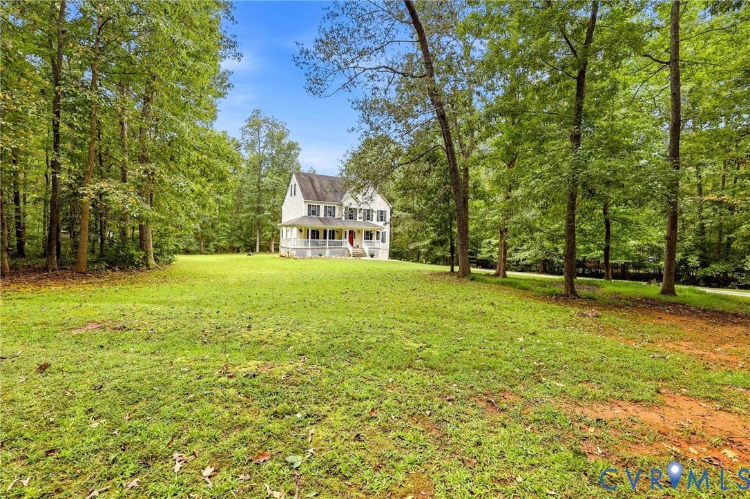 Expansive lawn surrounded by mature trees, offering a private setting for a two-story residence with a covered front porch and white balustrade