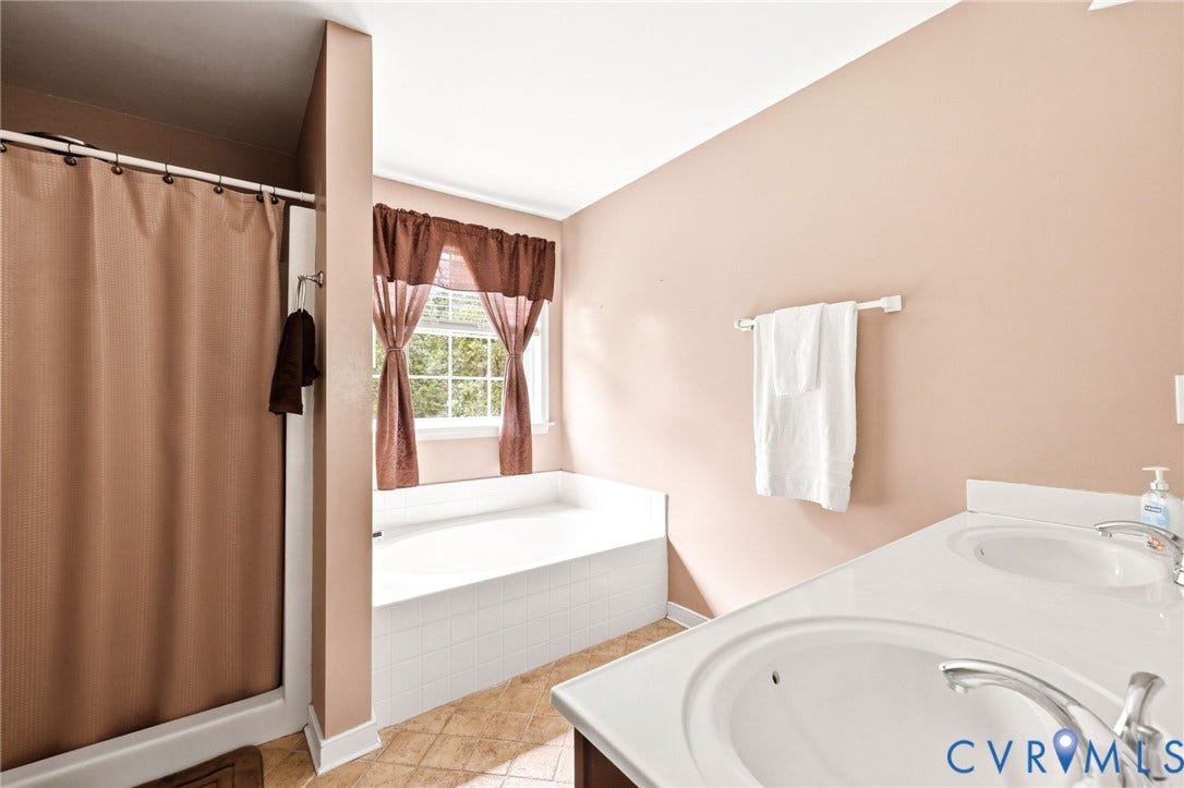 Dual vanity with integrated sinks, a built-in tub, separate shower stall, and a window for natural light