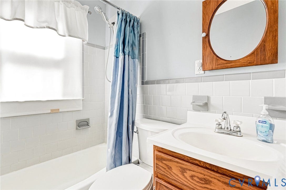Bathroom featuring a tile shower surround, a built-in bathtub, a vanity with wood-finish cabinetry, with a round mirror with a wood-finish frame.