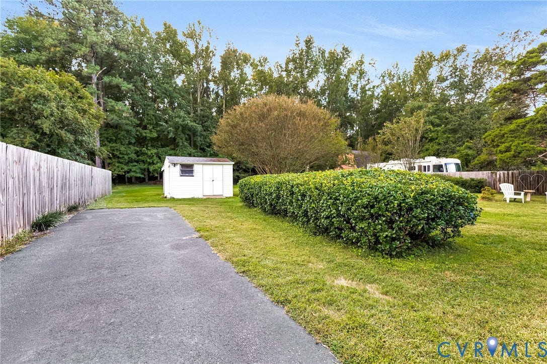 Back yard with privacy fencing and a manicured hedge, mature trees, and an asphalt driveway