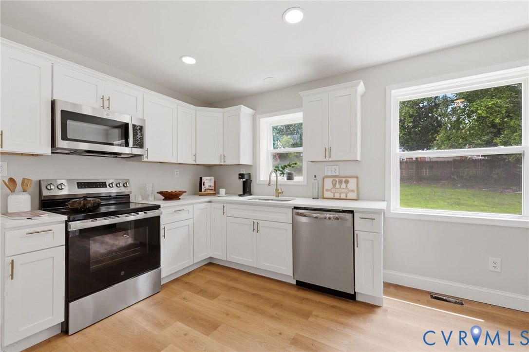 White cabinetry, stainless steel appliances, light wood-finish flooring, recessed lighting, and ample natural light