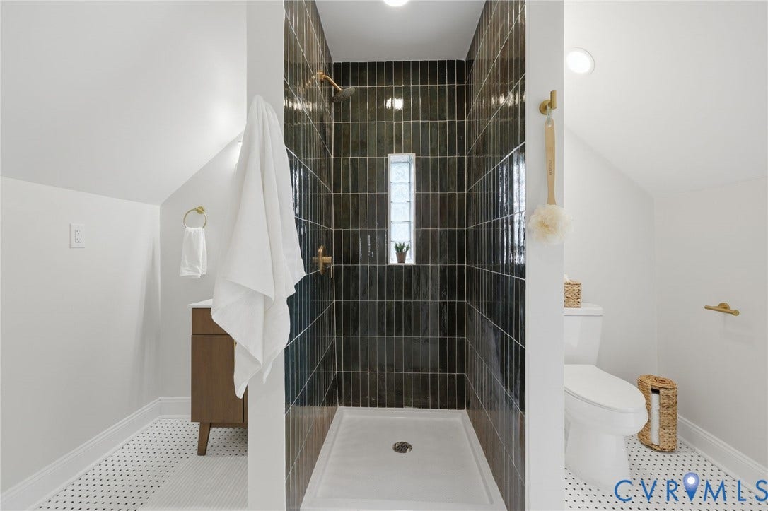 Tiled shower with vertical dark tile and a window, paired with a white vanity featuring a wood-finish cabinet and a white basin