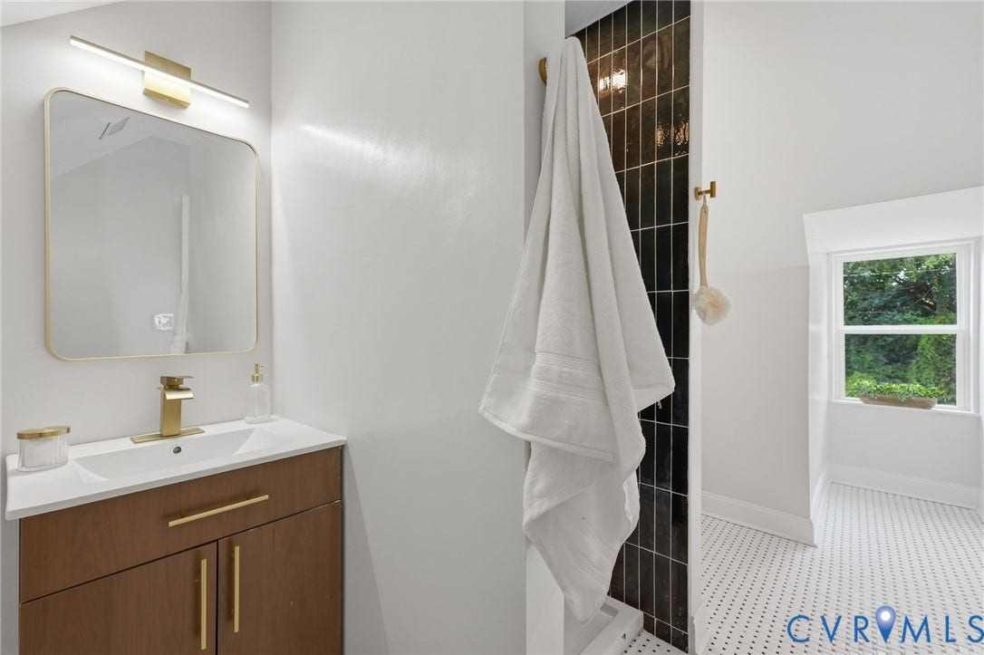 Bathroom featuring a wood-finish vanity with an integrated white sink, a gold-framed mirror, and a sleek gold-tone wall-mounted light fixture