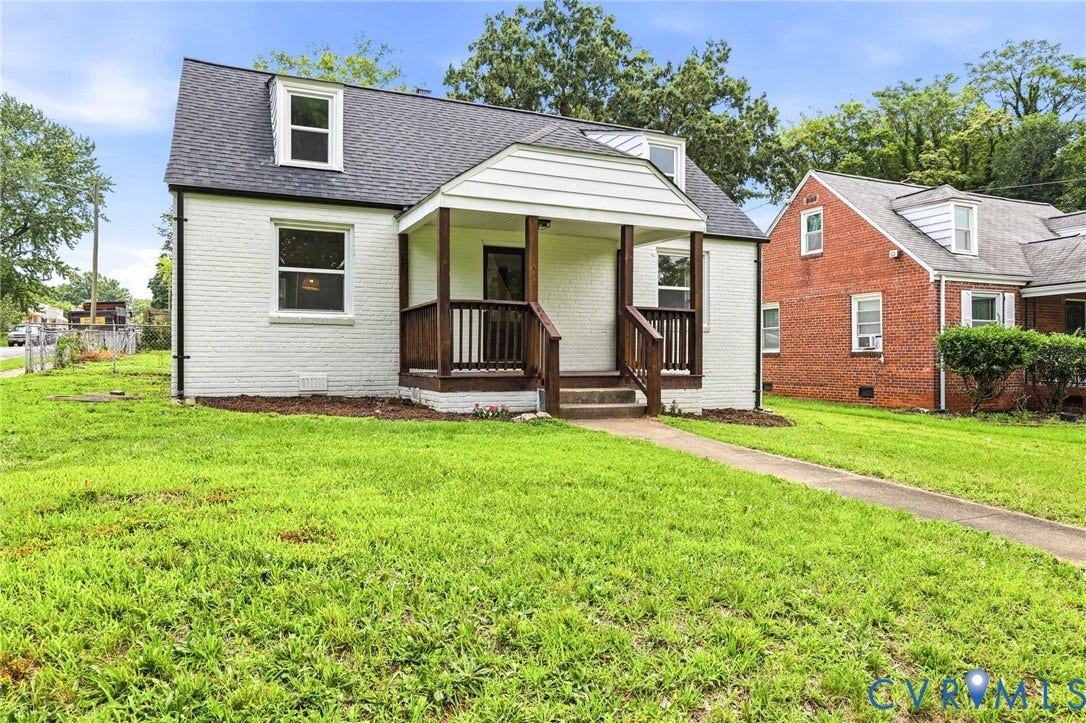 White painted brick exterior with a front porch, wood railing, and dormer windows