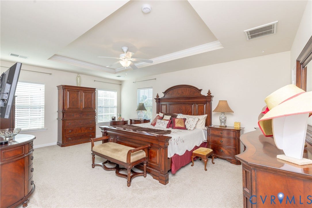 Tray ceiling with crown molding, ceiling fan, carpet flooring, and multiple windows with blinds