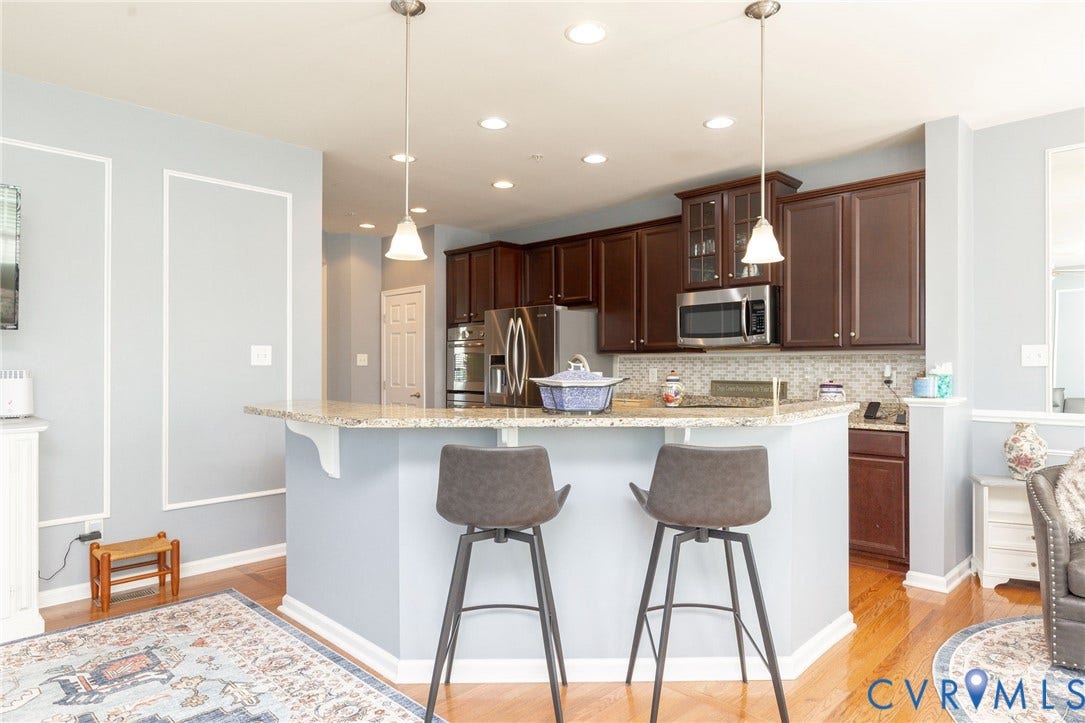 Kitchen featuring dark wood cabinetry, stainless steel appliances, a mosaic tile backsplash, a breakfast bar with a granite-style countertop, and recessed lighting