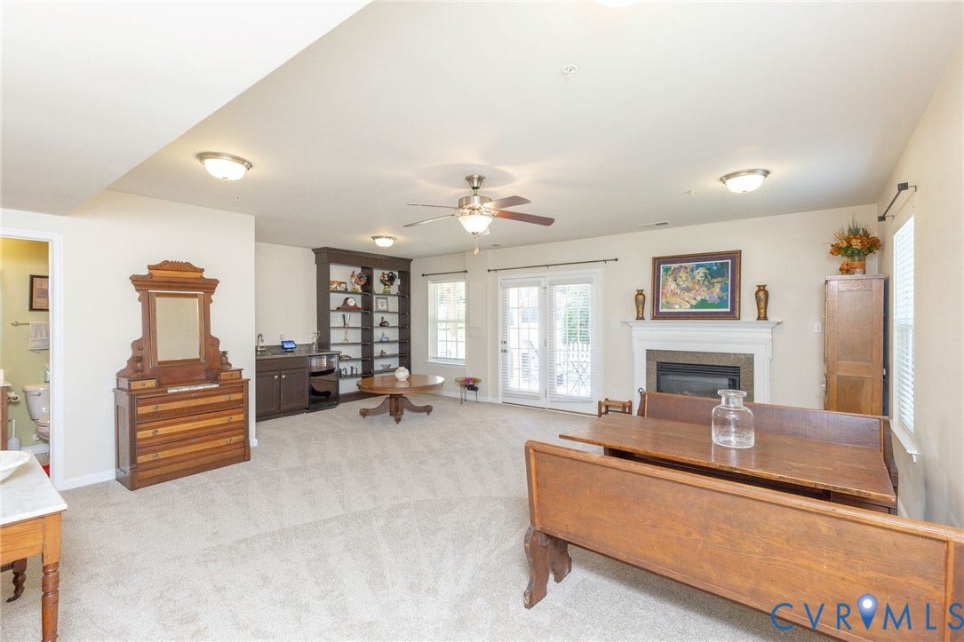 Carpeted room featuring a ceiling fan, fireplace with mantel, built-in shelving, and double glass doors