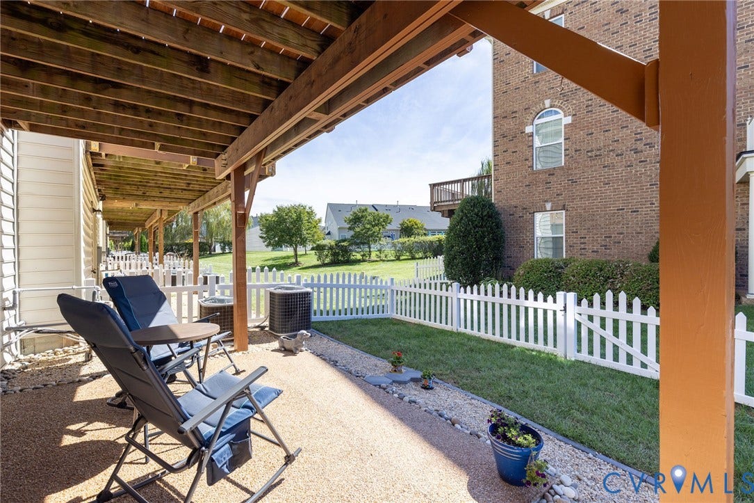Covered patio with a textured concrete surface, fenced lawn area, and mature landscaping